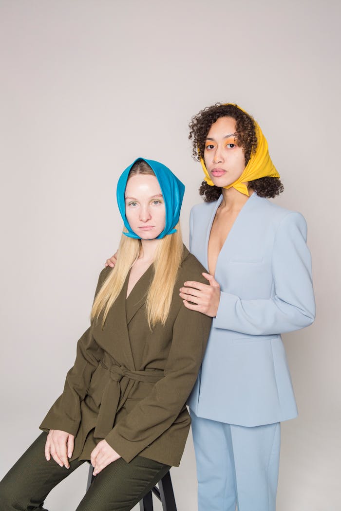 services-04 Confident young multiethnic girlfriends wearing jackets and colorful bandanas on head while looking at camera on gray background in light studio
